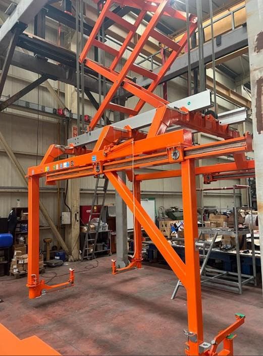 Fabricated orange steel gantry lifting frame in a production workshop