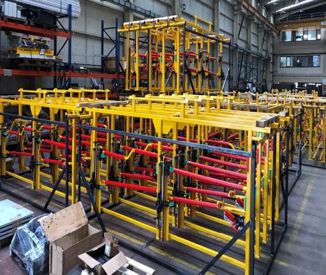 Fabricated yellow steel clamping frames with red hydraulic components in a workshop