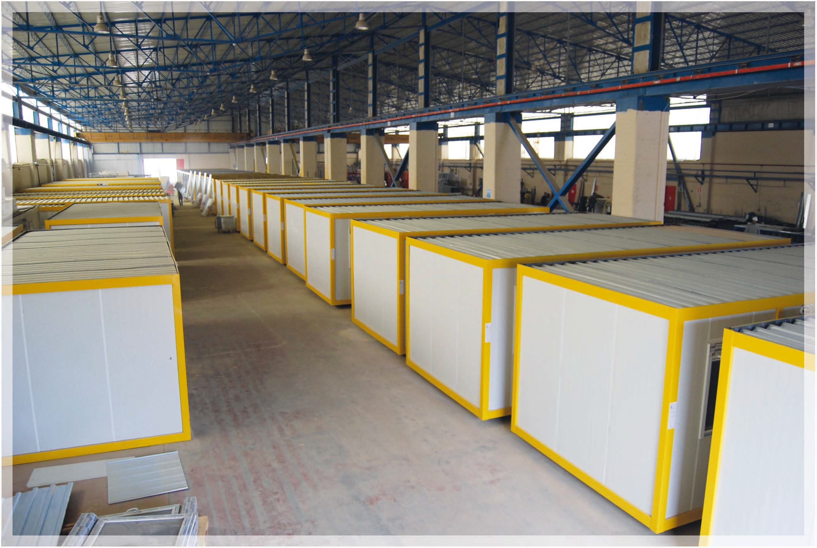Rows of finished prefabricated container units with yellow trim inside a factory hall