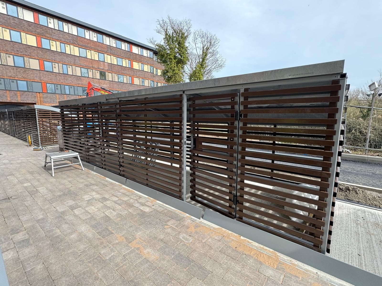 Covered bicycle shelter with slatted wood-effect cladding installed outside an office building