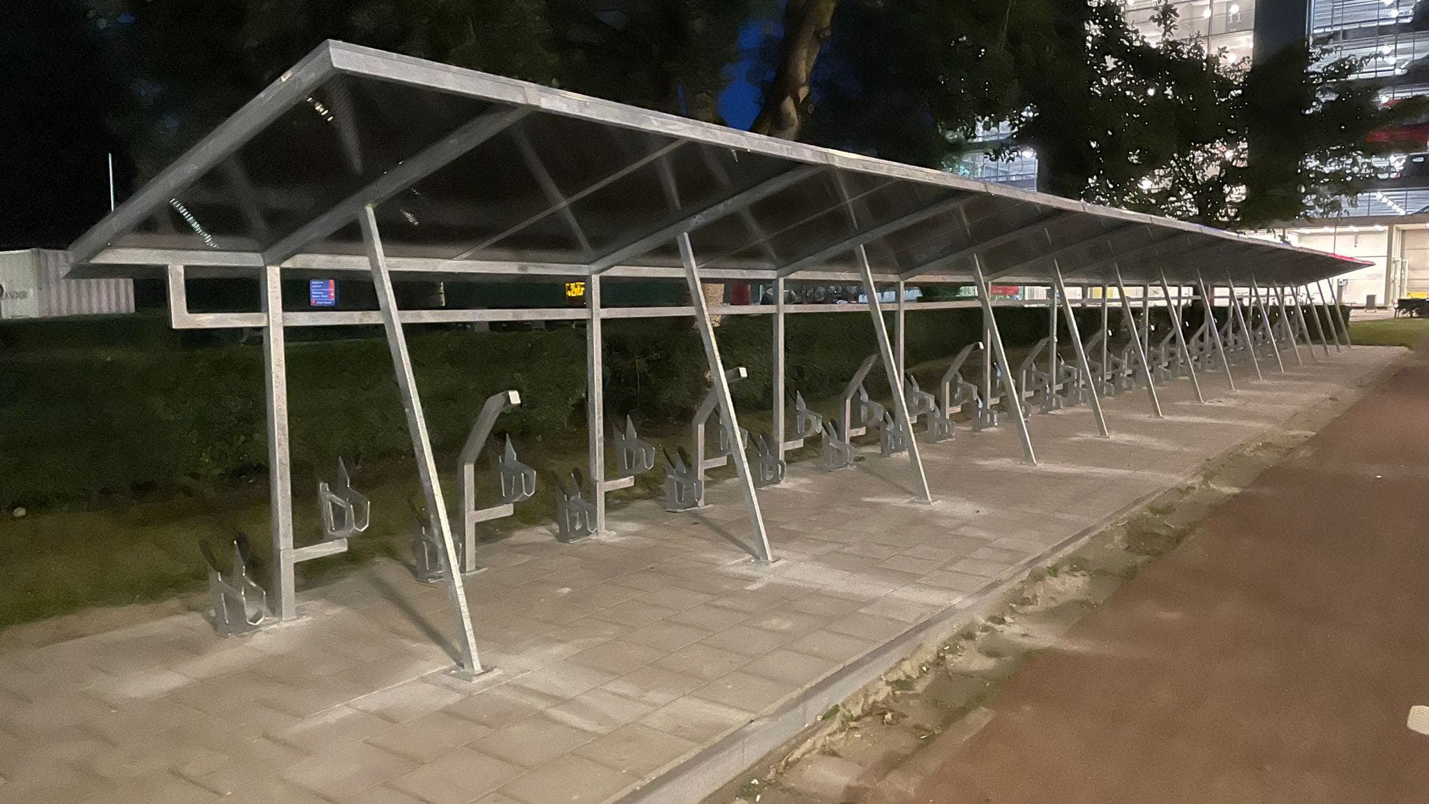 Long covered bicycle parking shelter with a raised canopy, photographed at night