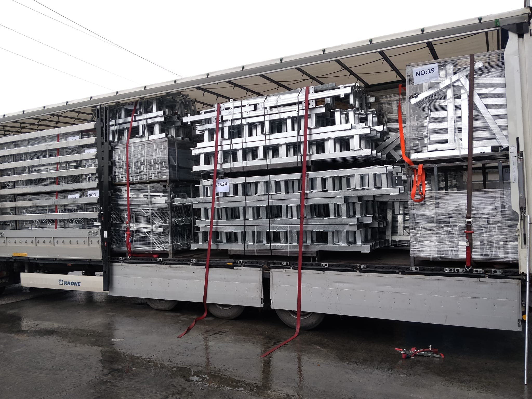 Flatbed trailer loaded with numbered bundles of galvanized steel beams and frames