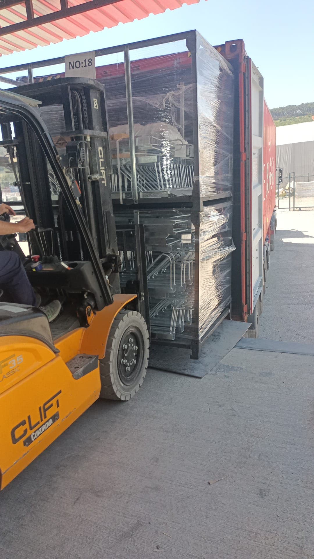 Forklift loading a shrink-wrapped pallet of steel components into a shipping container