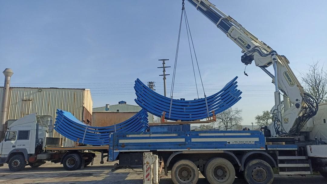 Mobile crane loading large curved blue-painted steel structural arches onto a flatbed truck