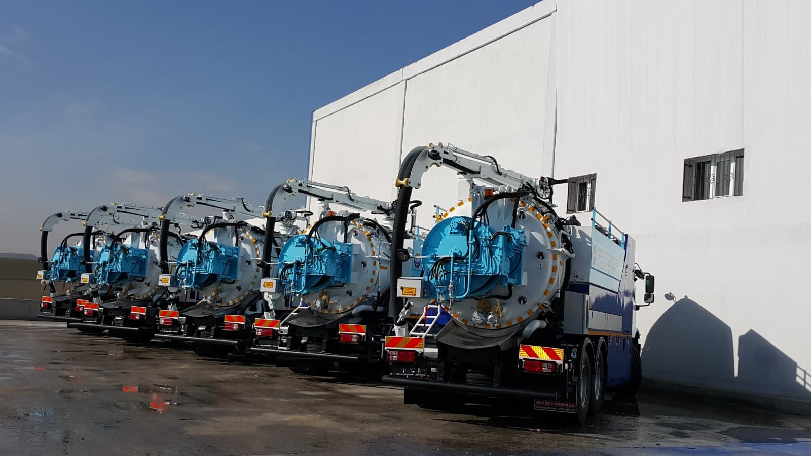 Row of five blue vacuum tanker trucks parked outside a facility