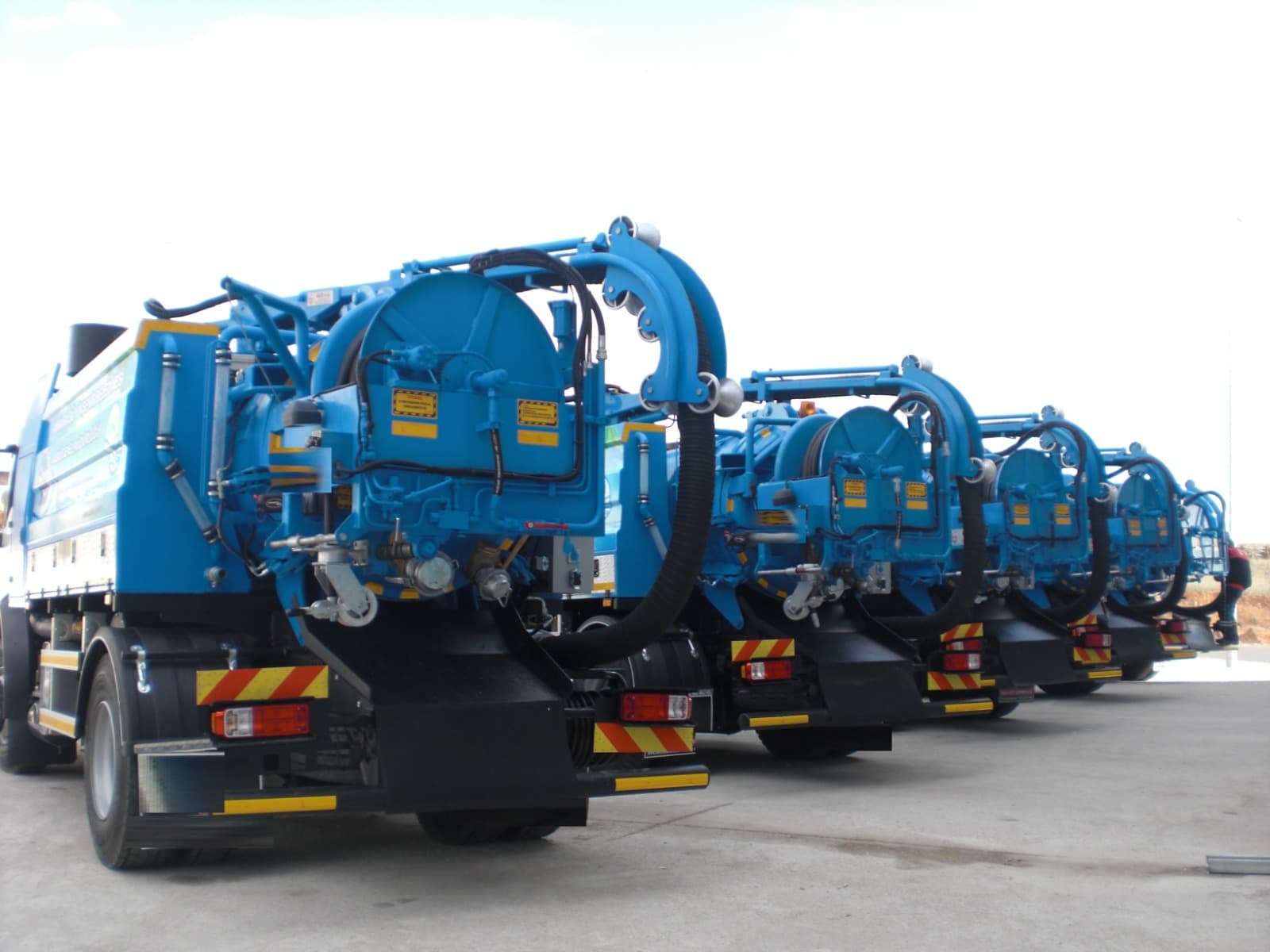 Rear view of a lineup of blue vacuum tanker trucks with hose reels