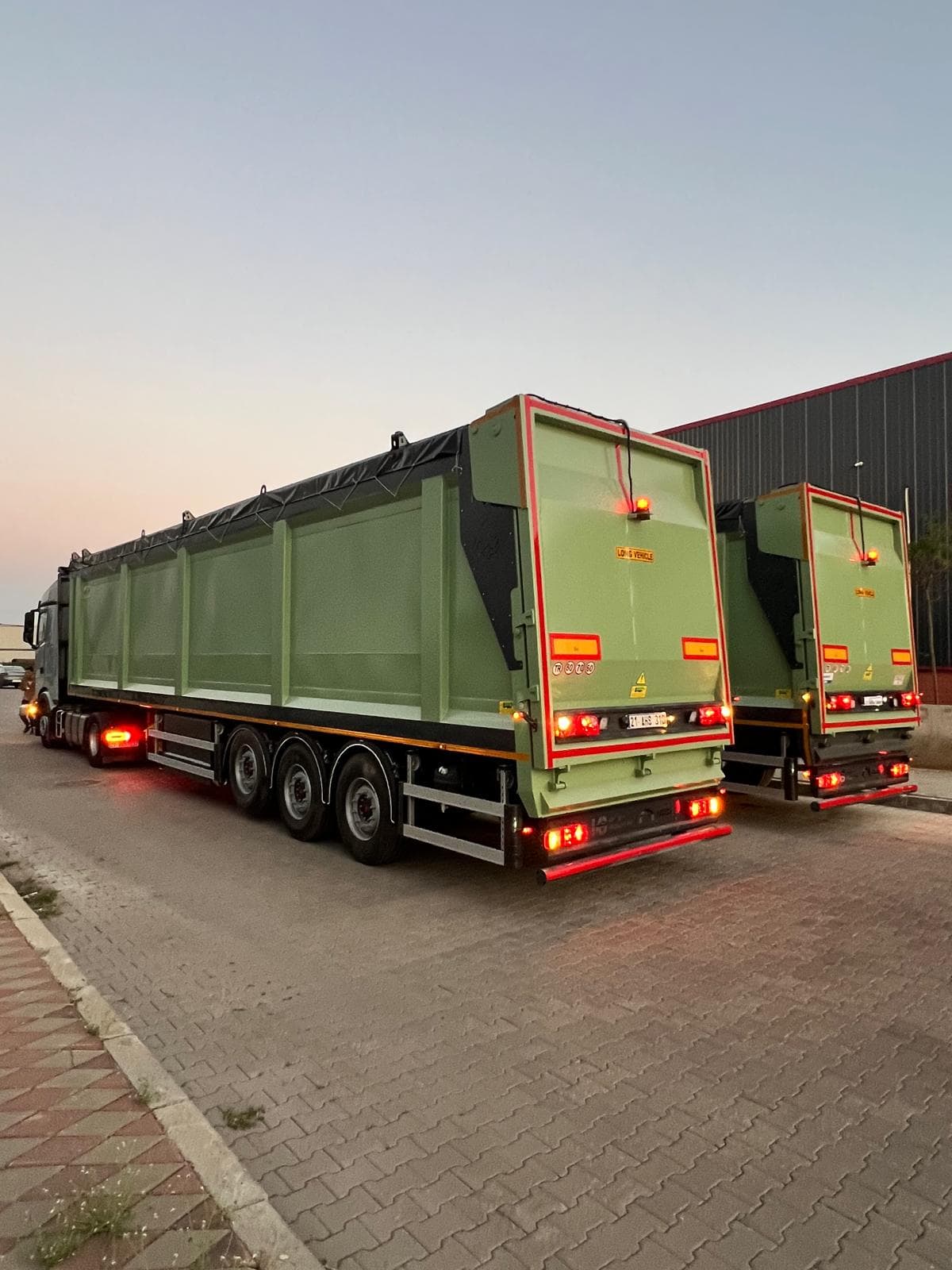 Two long green tipper trailers hitched to a truck at dusk