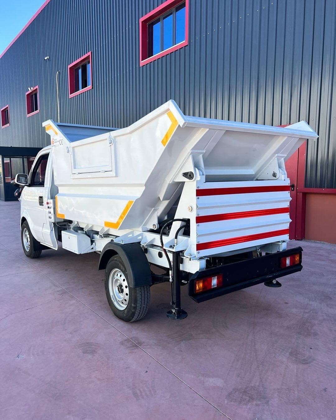 White tipper truck body with a striped tailgate mounted on a light truck chassis